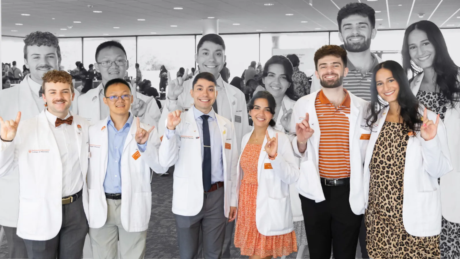 A group of Texas Pharmacy students at the white coat ceremony. They are holding up the "Hook 'em" hand gesture and smiling to camera.