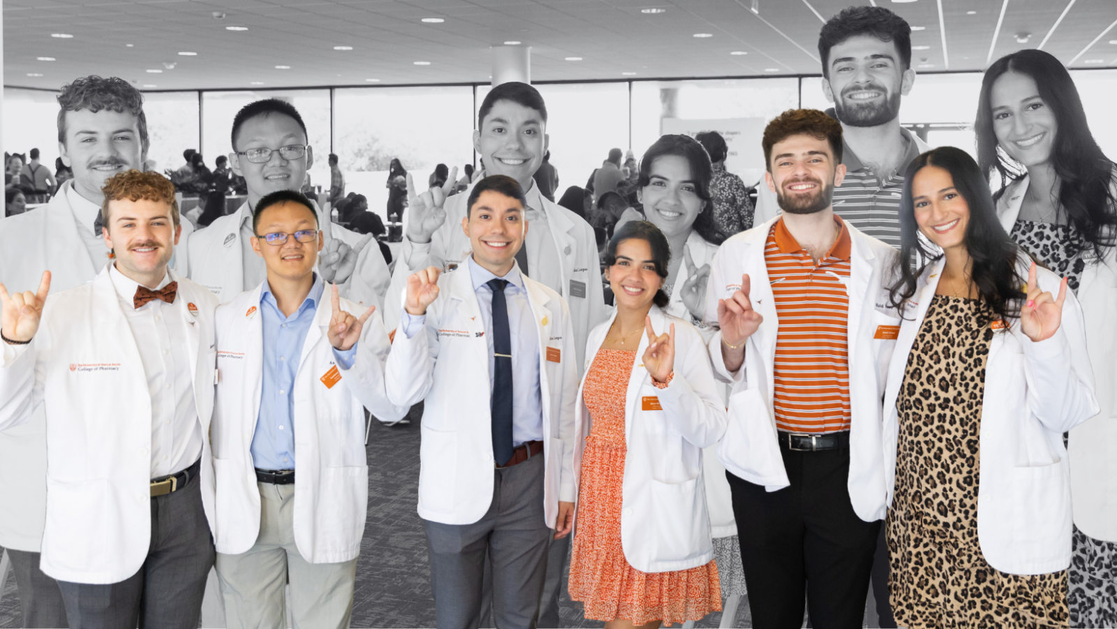 A group of Texas Pharmacy students at the white coat ceremony. They are holding up the "Hook 'em" hand gesture and smiling to camera.