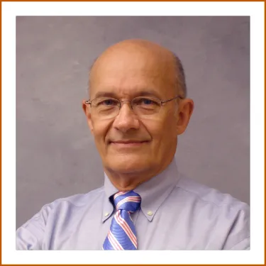 A Headshot of Dr. Carl Erickson. Dr. Erickson is wearing glasses, a striped pink and blue tie and light button-up shirt.