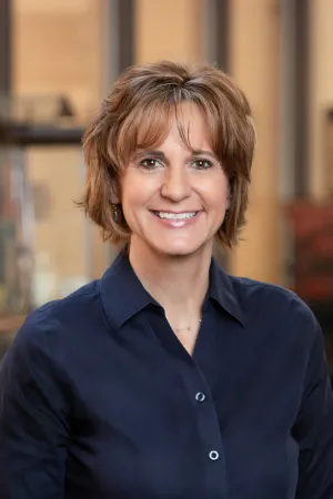 Headshot of Dean Renee Acosta. She is wearing a navy button down collared shirt and is smily brightly to camera. 