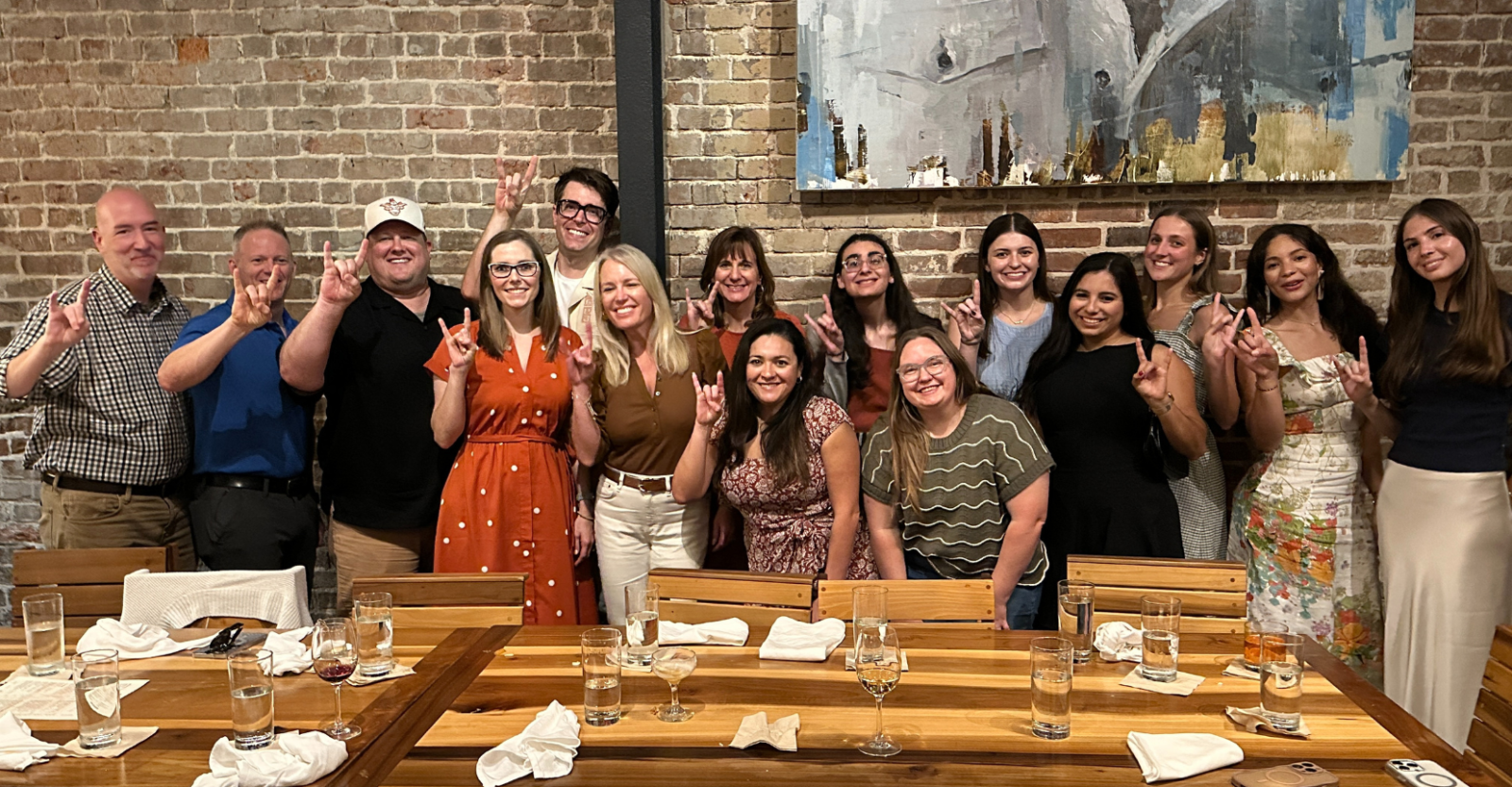 A large group of Texas Pharmacy students, faculty, staff and friends pose together at a celebratory dinner. Everyone is smiling and holding up the "Hook 'em Horns" hand gesture.