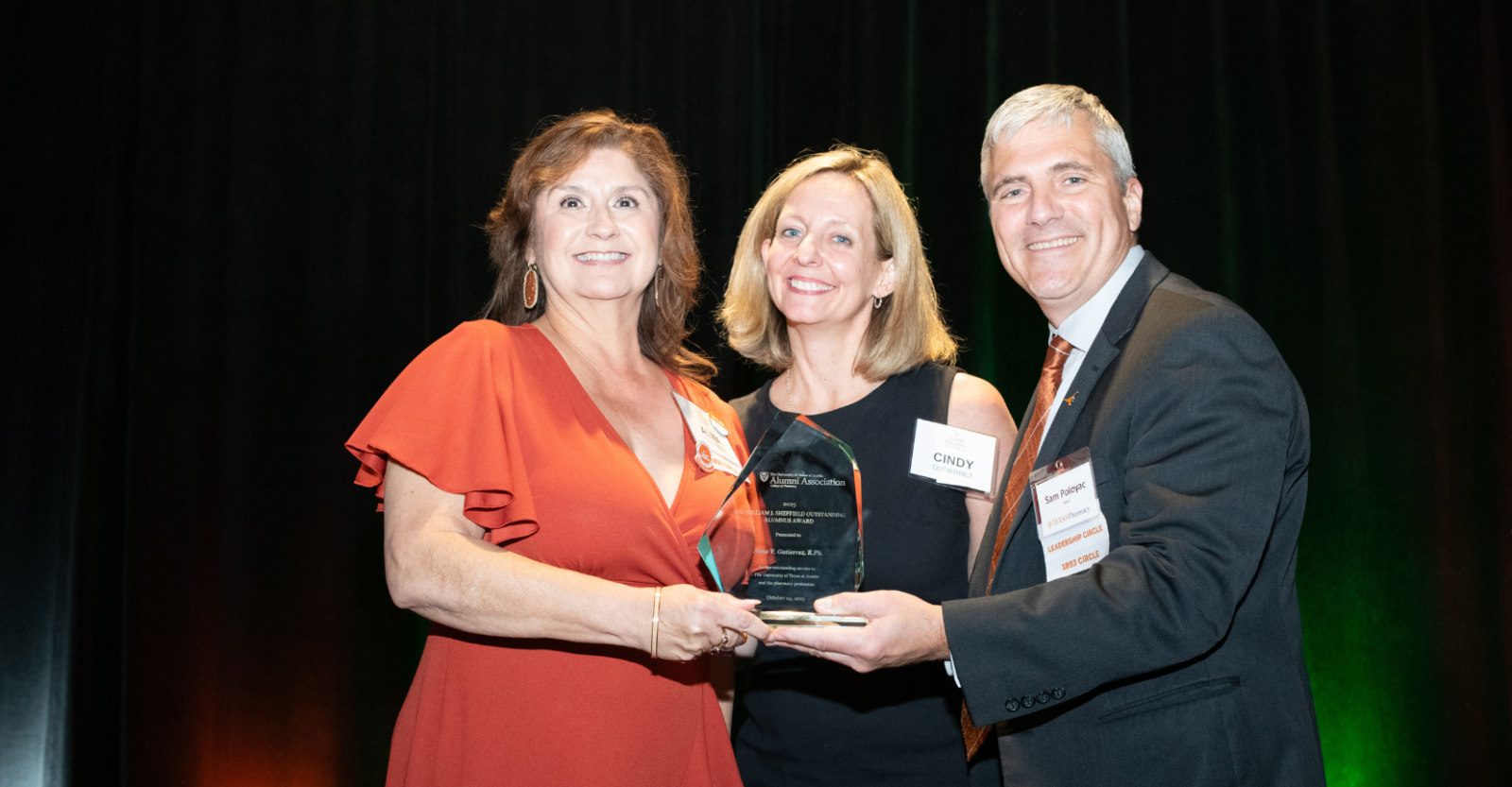 Two female alumni standing with Dean Poloyac on stage. One holding an award.