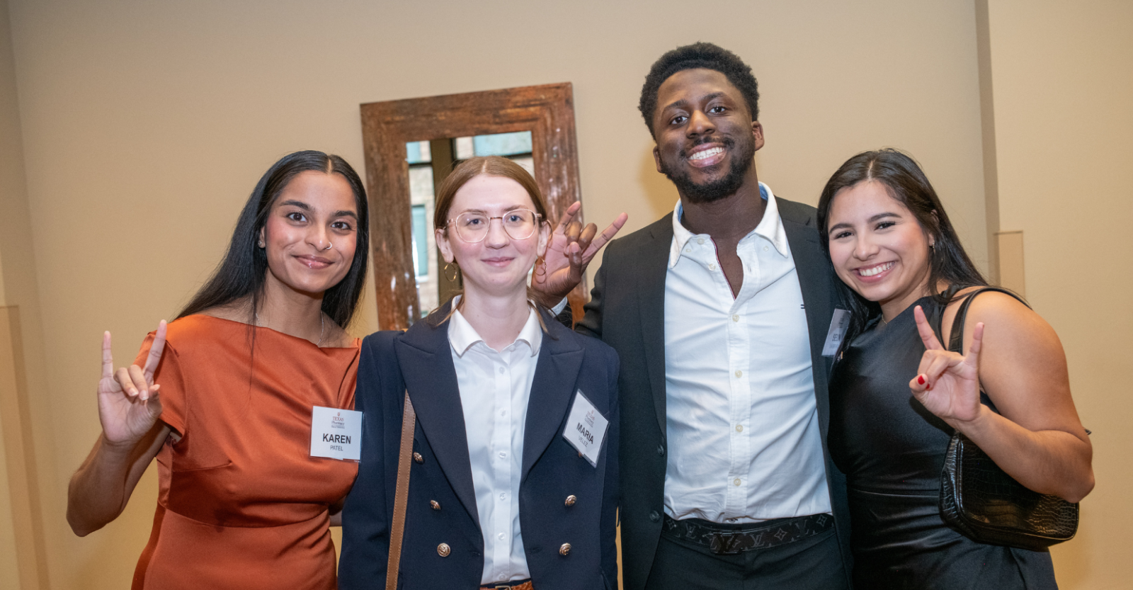 Four young Texas Pharmacy students and alumni posing together with the "Hook 'em Horns" hand gesture.