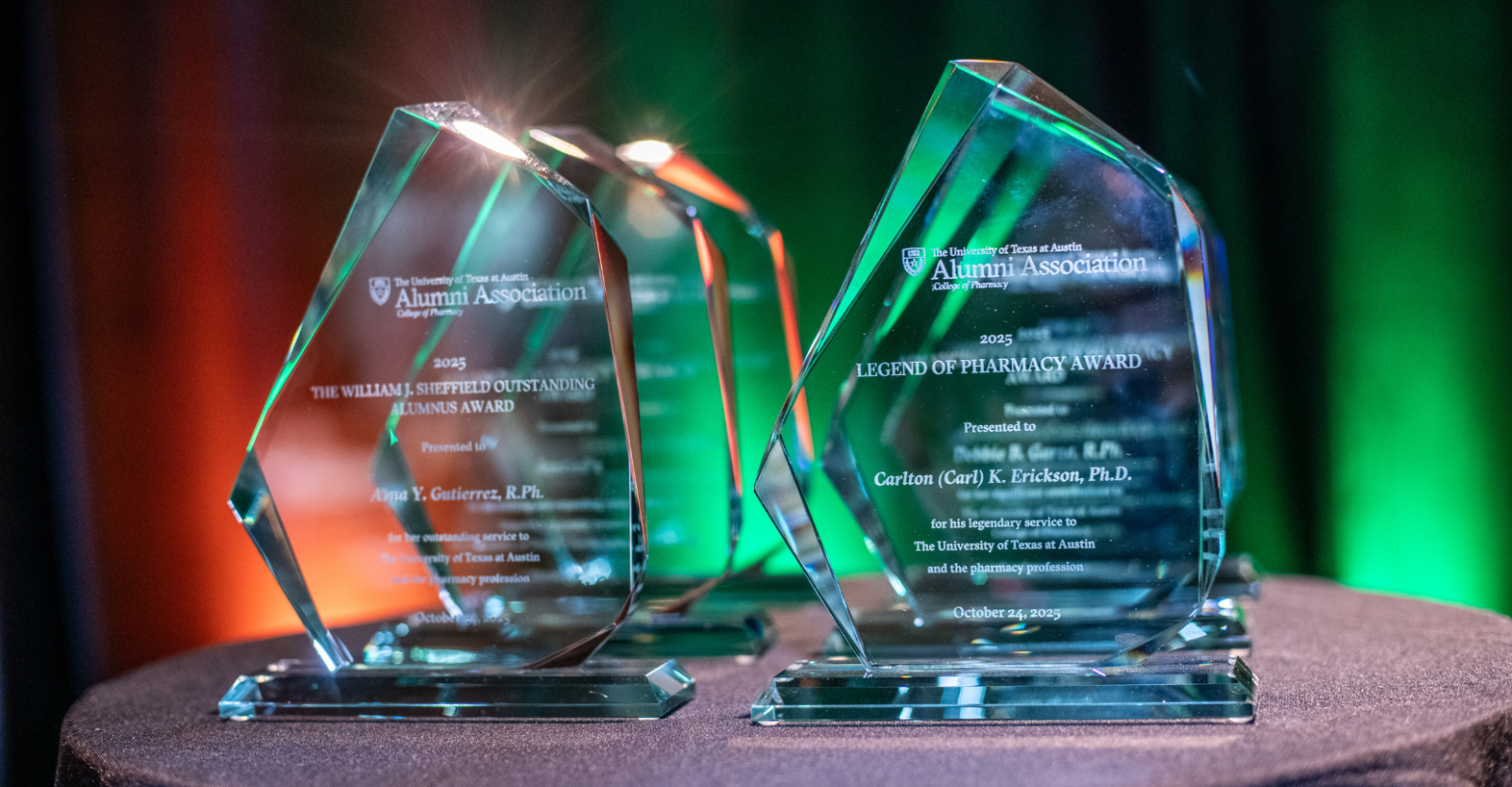 Engraved glass trophies sit atop a black table cloth in display at an event.