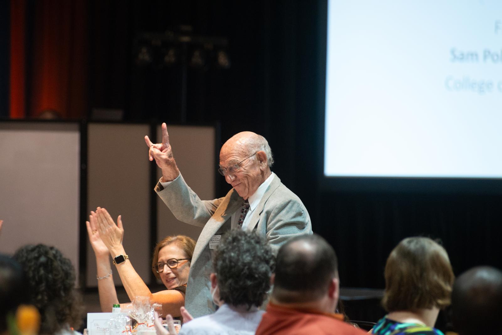 A man wearing a suit and giving the Hook 'em Horns hand gesture.
