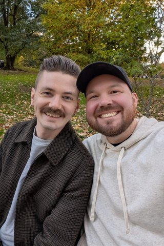 A couple posing together for a selfie on a bench in a green park.
