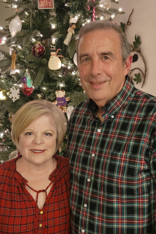 A senior couple pose together for a photo in front of a decorated Christmas tree.