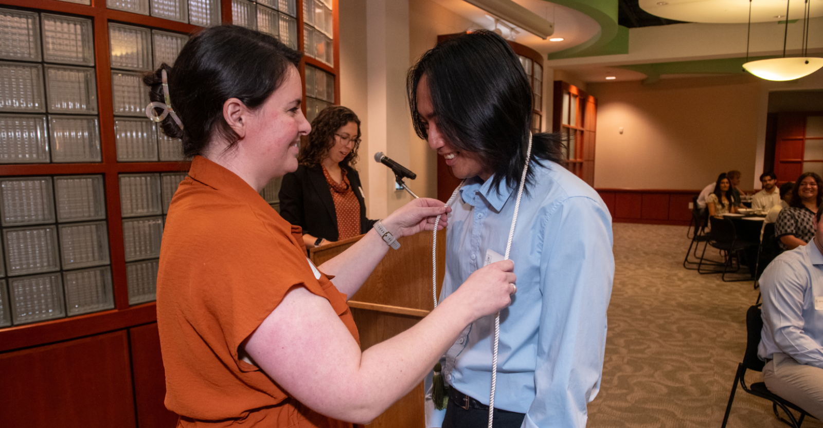 A student being presented academic cords at a college event in an event hall.