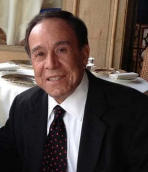 Headshot of David Garcia. David is wearing a dark suit, white collared shirt and a blue and red tie. He smiles to camera.
