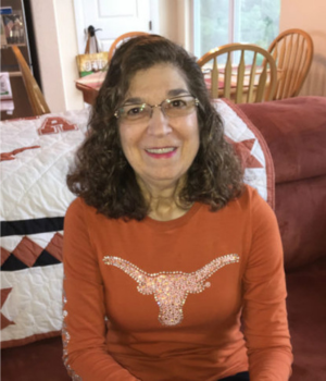 Nora Francis sits and smiles warmly to camera wearing a burnt orange long-sleeve shirt with the UT Austin Longhorn logo bedazzled in the center.