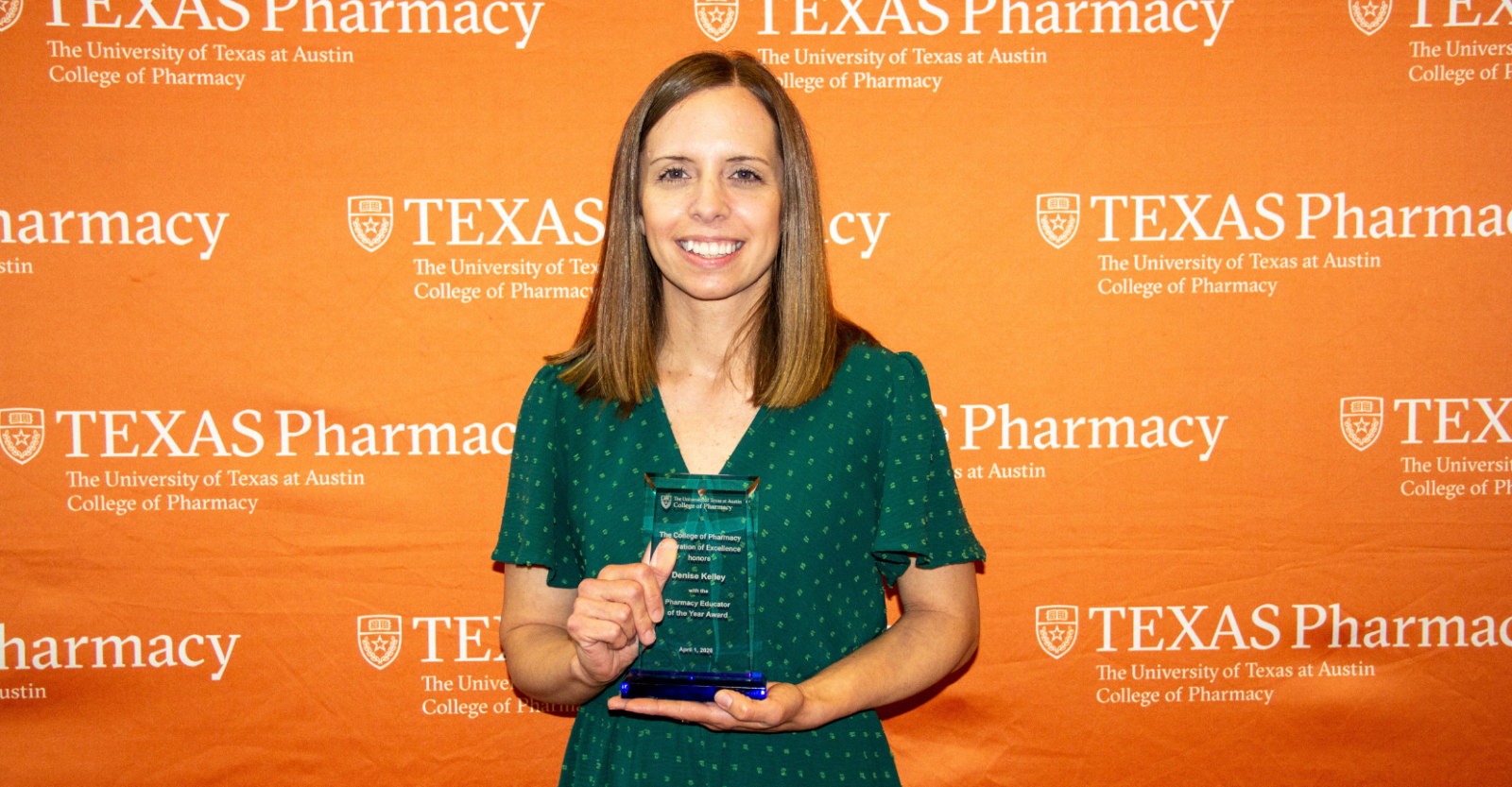 Dr. Denise Kelley holding a glass award that reads "Pharmacy Educator of the Year". She is wearing a green dress and is smiling brightly to camera standing in front of a burnt orange and Texas Pharmacy-branded step and repeat backdrop.