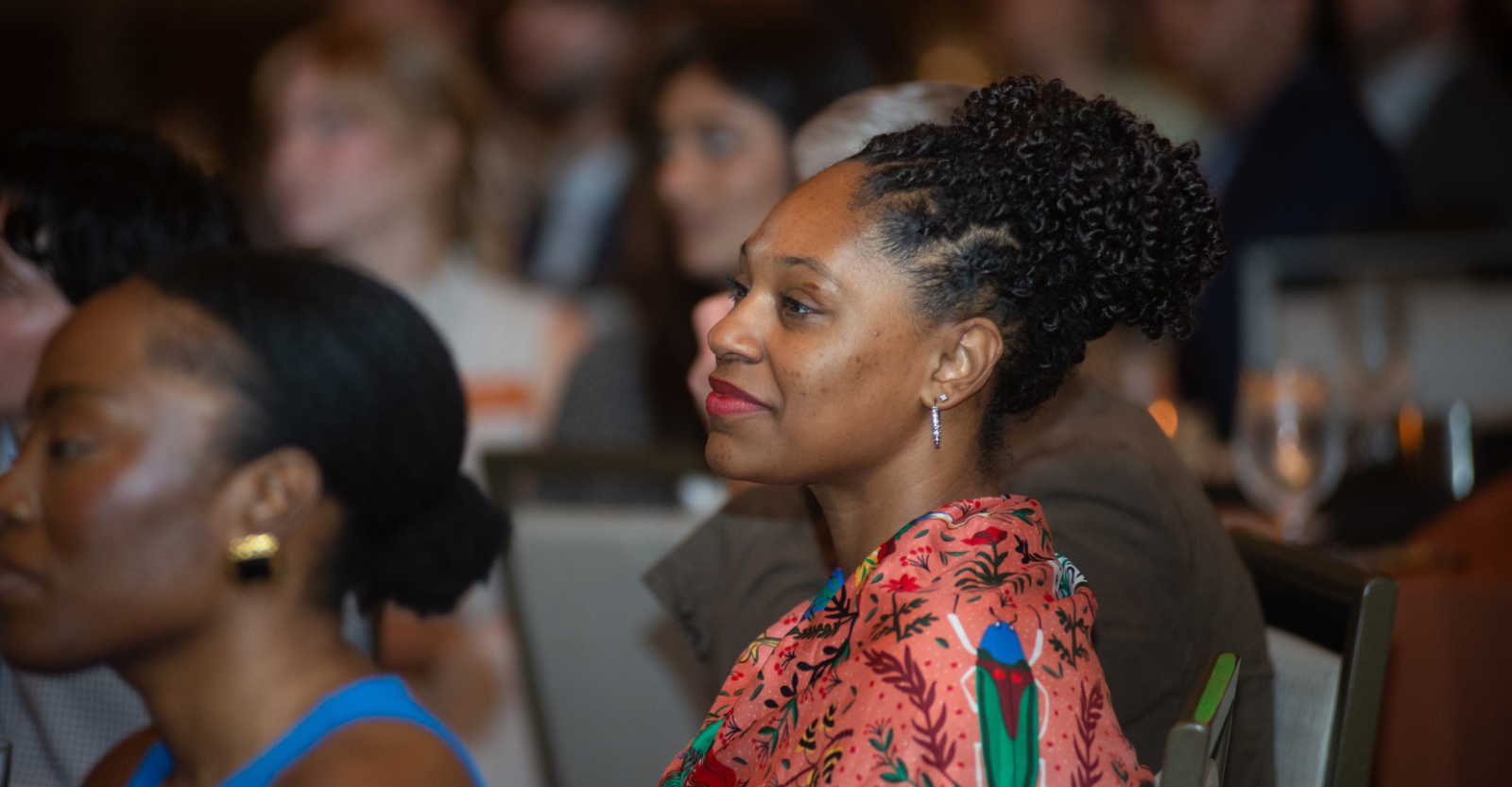 Graduate student, Alexcia, sitting and listening attentively to a speaker. She is wearing a colorful, silk scarf around her shoulders.