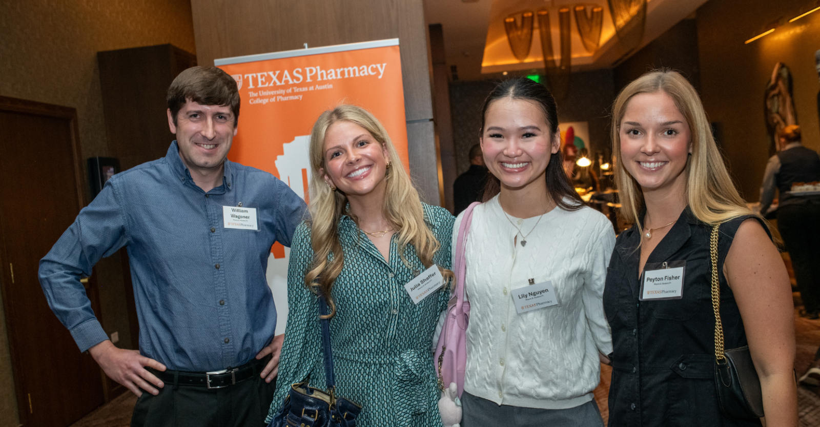 Four people dressed in business casual attire smile brightly to camera at a UT Austin College of Pharmacy event.