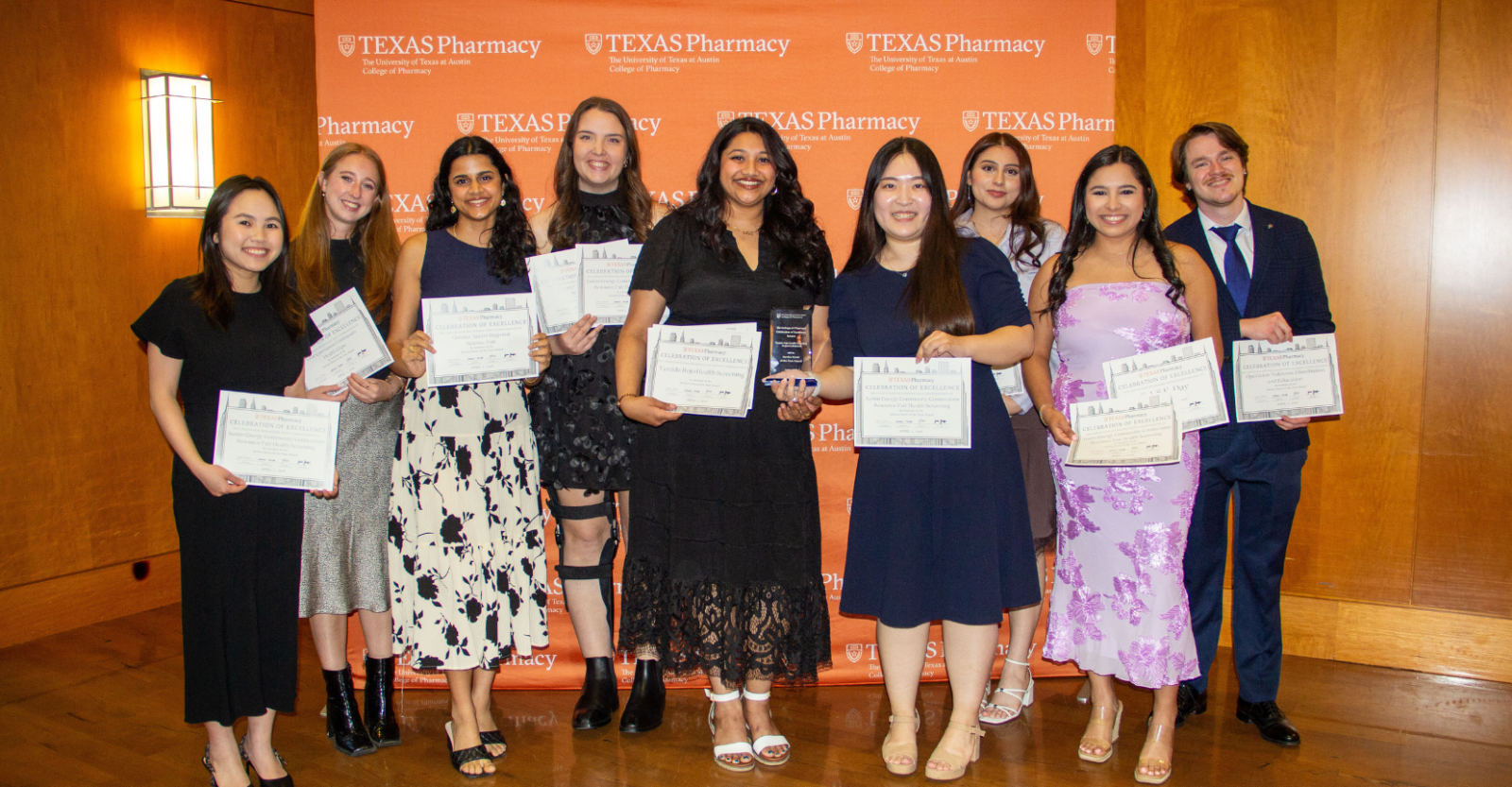 A group photo of students, dressed smartly at an award event, posing together holding awards and certificates.