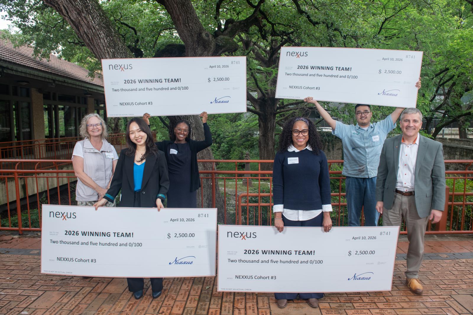 A group of people posing outside with large checks.