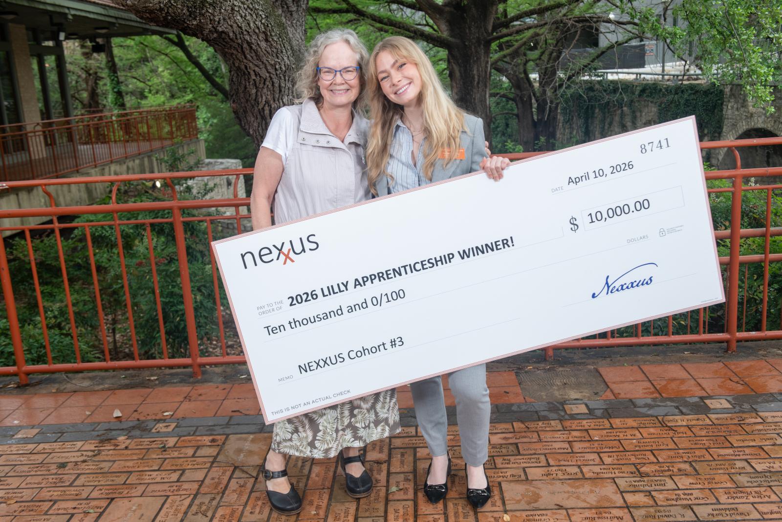 Two people posing outdoors with a large check.