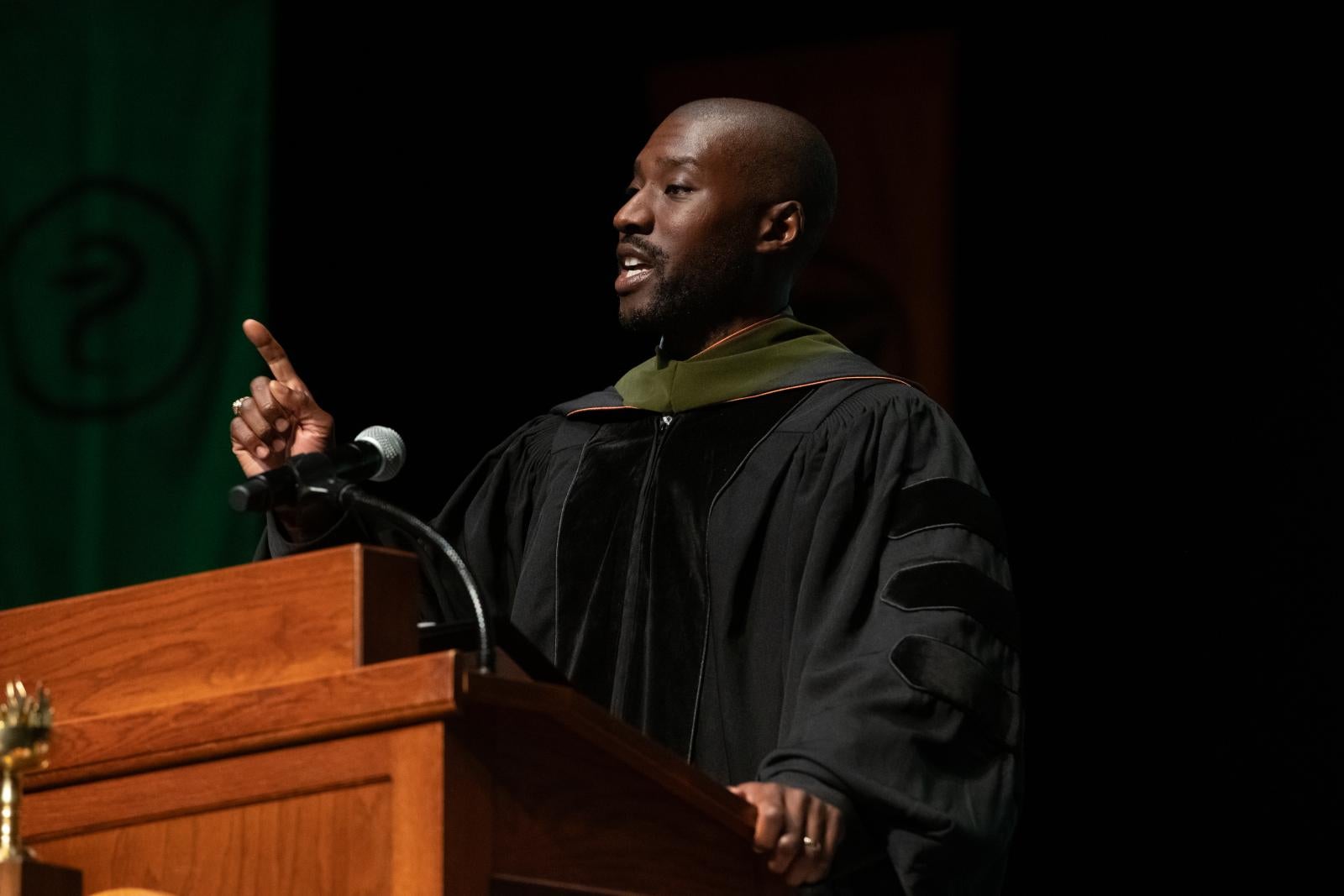 A man pointing while giving a graduation speech.