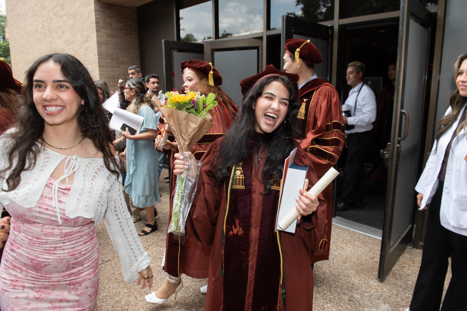 A graduate holding flowers and smiling.