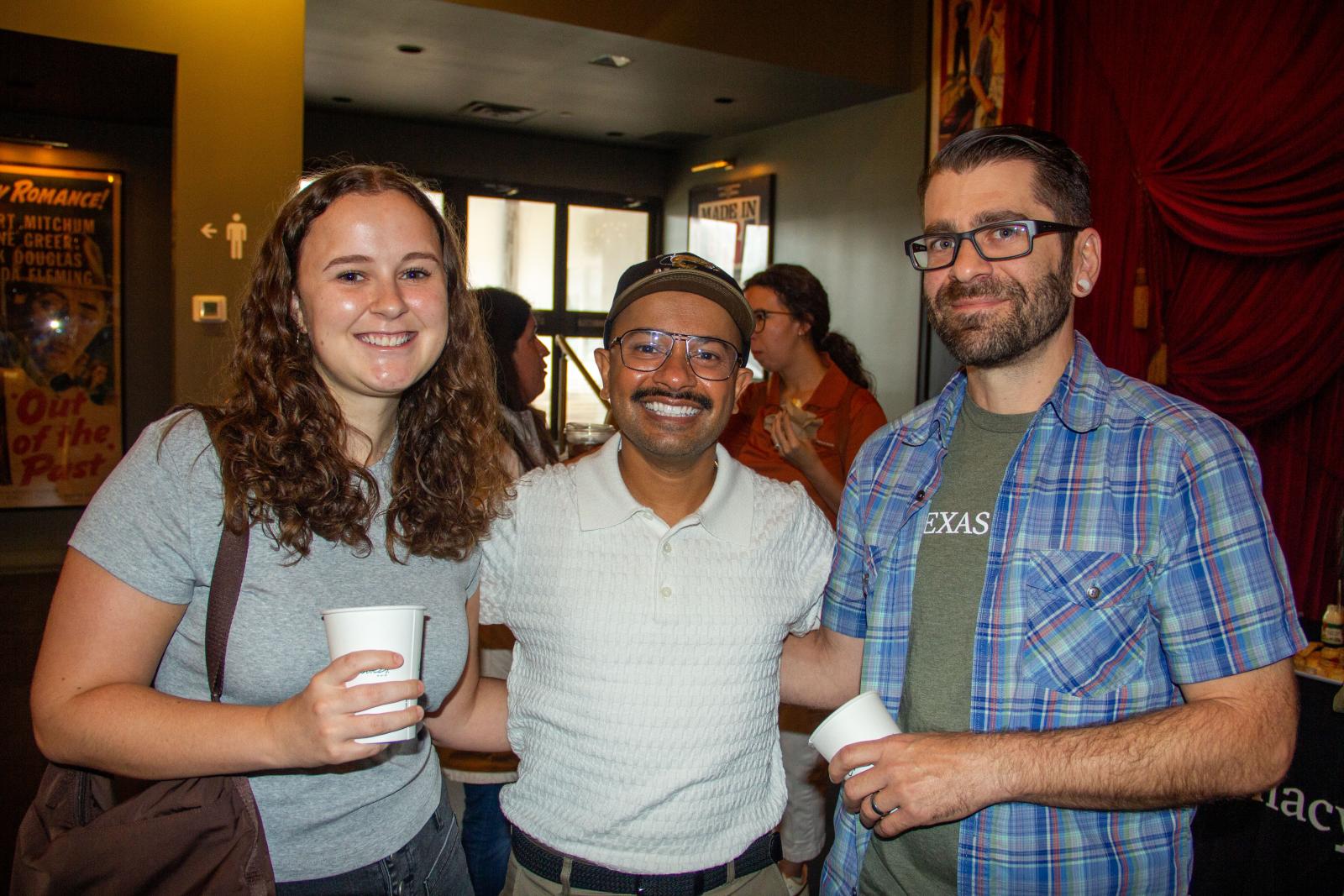 Three people smiling in a movie theater lobby.