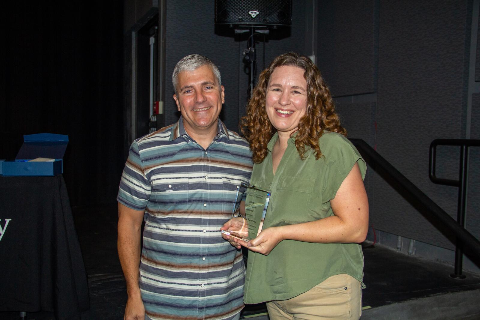 A man and a woman smiling while holding an award.