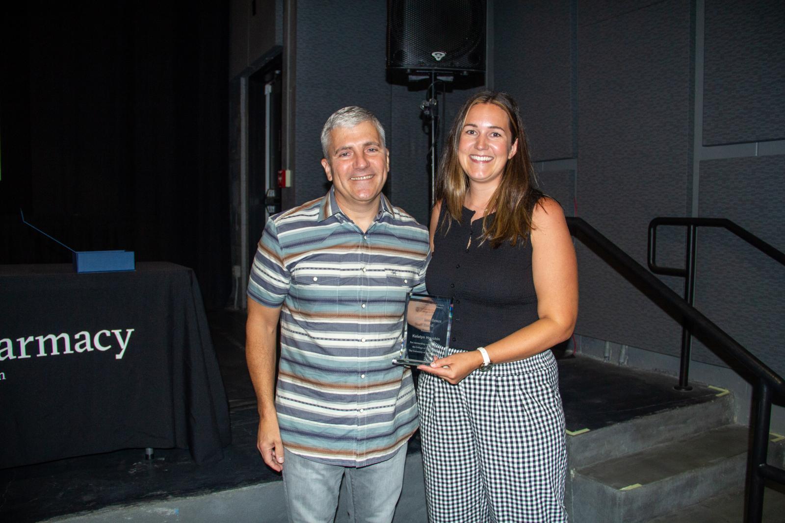 A man and a woman smiling while holding an award.