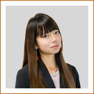 Headshot of student pharmacist Elaine. She has long dark hair and is wearing a dark blazer over a light shirt. She smiles softly to camera.