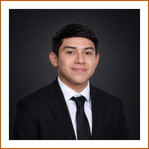 Headshot of student pharmacist Isaiah. He smiles softly to camera in front of a black backdrop, wearing a black suit jacket, tie and white shirt.