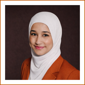 Headshot of student pharmacist Khadijah. She is wearing a burnt orange blazer and a white head covering, smiling softly to camera.