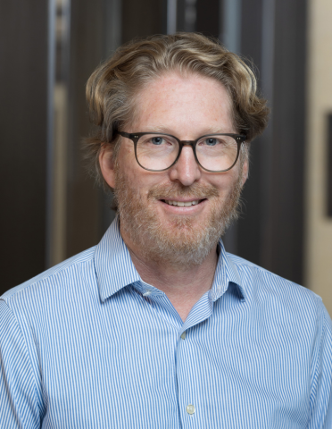 Professional headshot of Dr. Smyth with glasses, blonde hair, a beard and blue shirt.