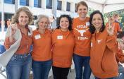 Five Pharmacy alums outdoors wearing burnt orange and giving hook em horns hand sign at Homecoming Tailgate