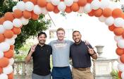Three Pharmacy students standing under balloon arch and giving hook em horns hand sign