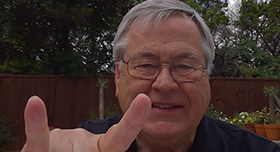 A man smiling and giving the Hook 'em Horns hand gesture.