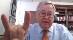 A man with glasses throwing up the Hook 'em Horns hand gesture