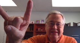 A man smiling and giving the Hook 'em Horns hand gesture.