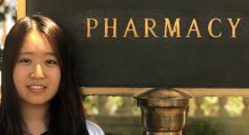 A woman smiling in front of a sign that says "Pharmacy."