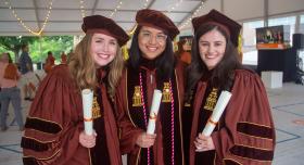Three women in regalia holding diploma scrolls.