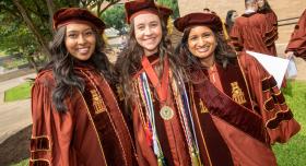 Three female College of Pharmacy graduates smiling in regalia.