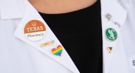 A white coat with a Texas Pharmacy, UTCOP and rainbow heart button.