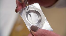 Two hands using tweezers to pull a thin transparent film from its foil packaging.