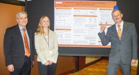 Three people standing in front of a research poster. One person is giving the Hook 'em Horns hand gesture.