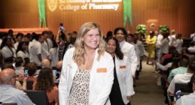 A blonde student wearing a white coat walking in the processional at the ceremony.