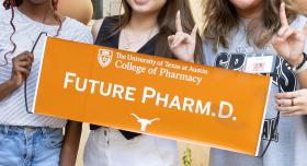 Three people giving the Hook 'em Horns hand gesture and holding a "Future Pharm.D." banner.