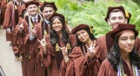 A group of graduates wearing regalia and giving the Hook 'em Horns.