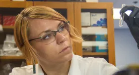 Someone in a lab white coat looking at a small test tube.