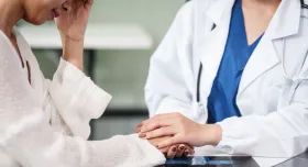 Stock image of a female physician holding the hand and comforting a female patient.