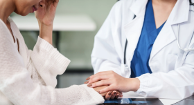 Stock image of a female physician holding the hand and comforting a female patient.