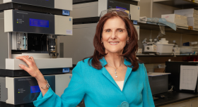 Photo of Dr. Janet Walkow. Walkow is standing in a lab wearing a blue button-up blouse and black pants. She is has shoulder-length brown hair and is smiling to camera.