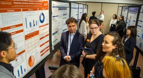 A group of people in a semicircle around a research poster.