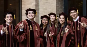A group of graduating students in their regalia giving the Hook 'em Horns.