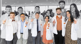 A group shot of Texas Pharmacy students at the white coat ceremony. They are holding up the "Hook 'em" hand gesture and smiling to camera.